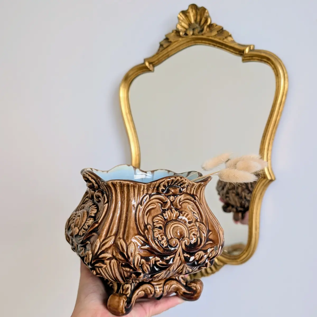 Cache-pot ancien en barbotine tenu en main devant un miroir doré d'époque.