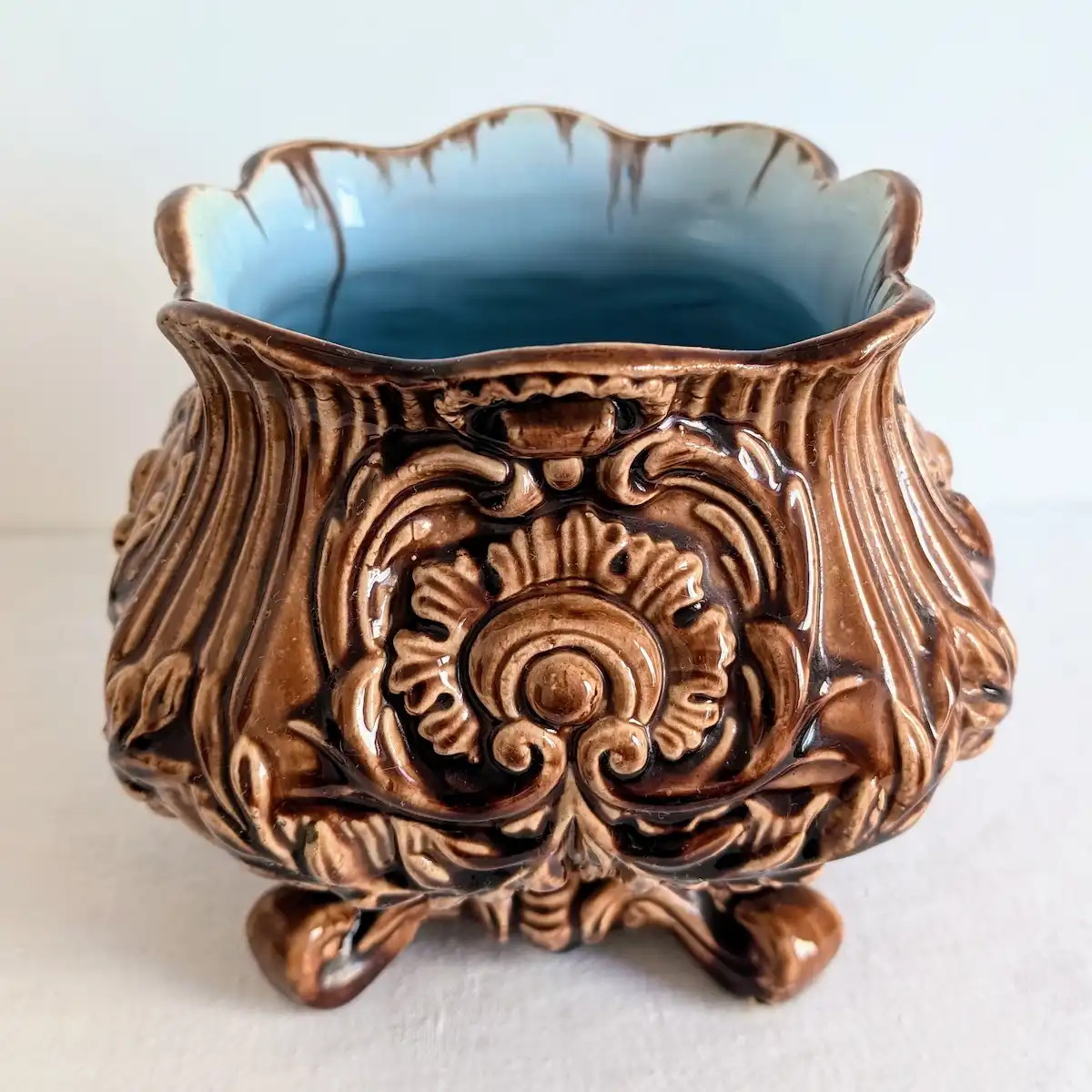 Cache-pot ancien en barbotine émaillée brun caramel à reliefs néo-baroques et pieds galbés.