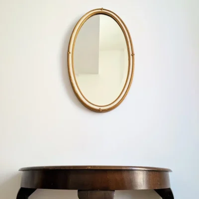 Miroir ancien ovale de coiffeuse biseauté doré posé au-dessus d'une console en bois