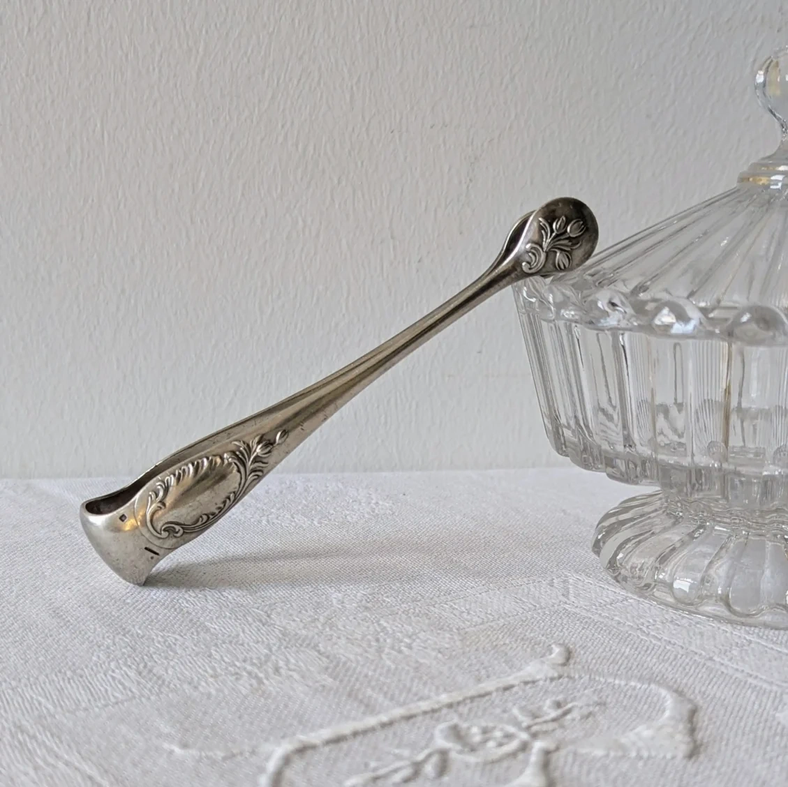 Pince à sucre Christofle motif Rocaille en métal argenté posée sur un sucrier en cristal