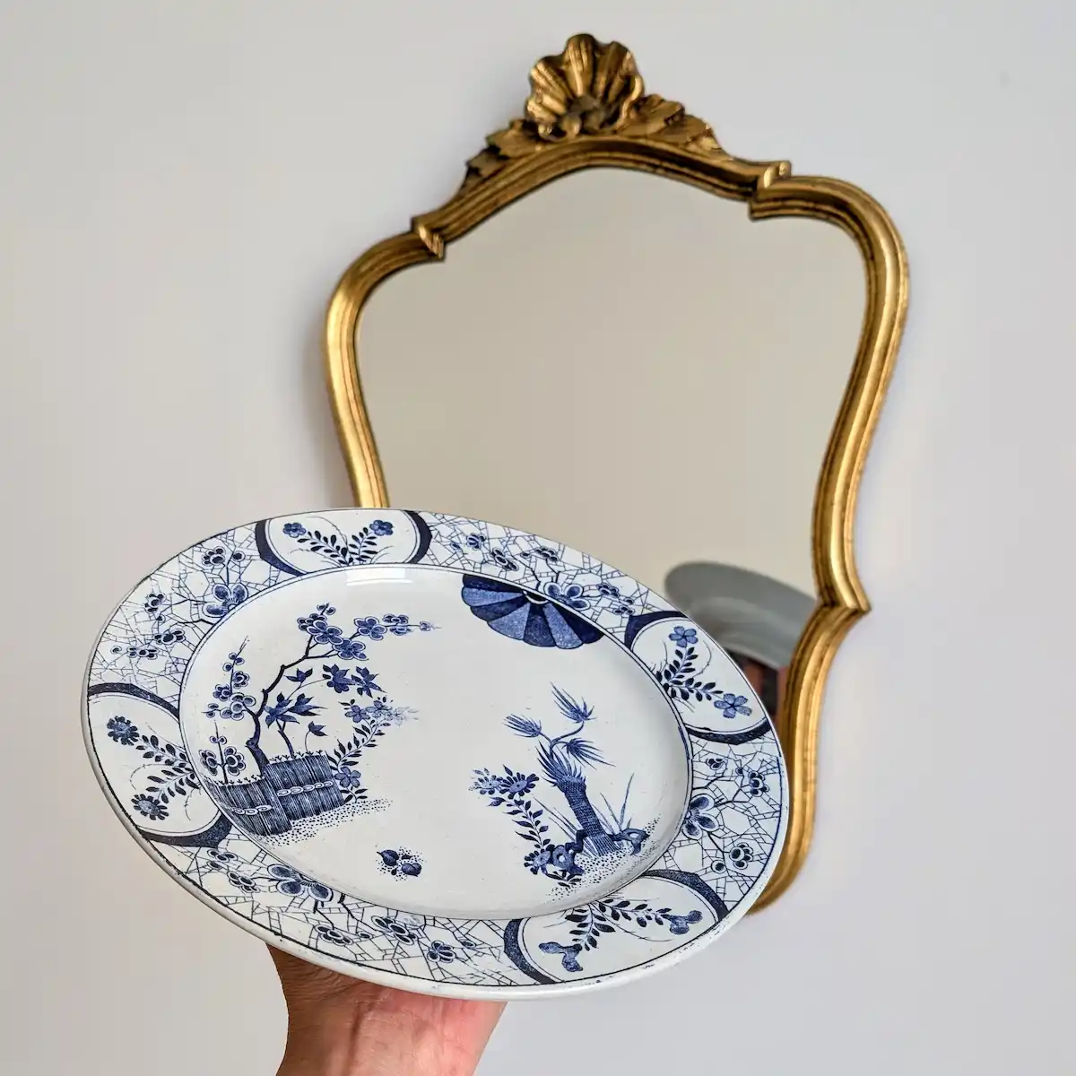 Plat ancien en faïence présenté à la main devant un miroir à parecloses doré