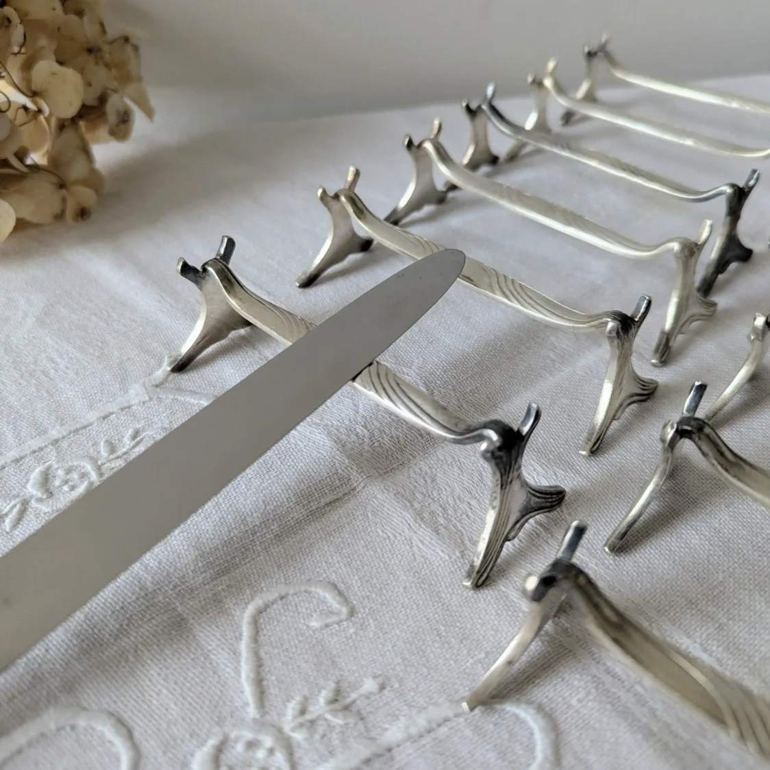 Série de porte-couteaux géométriques Christofle modèle Moderne 1912 alignés sur nappe blanche