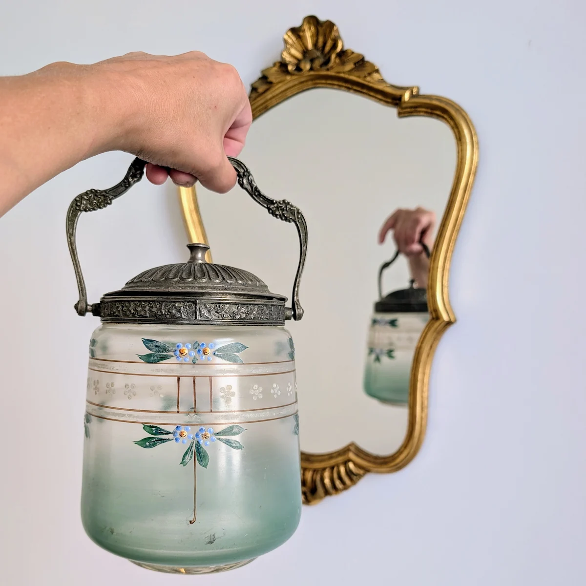 Prise en main par l'anse mobile d'un seau à biscuits vert d'eau devant miroir