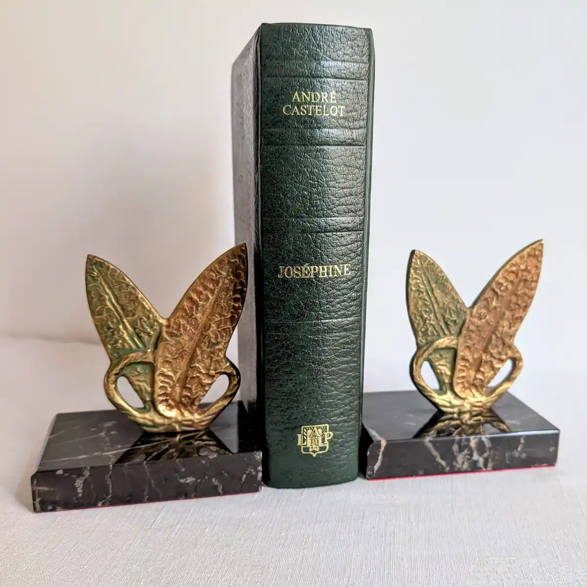 Paire de serre-livres vintage en marbre noir et métal doré retenant un livre relié
