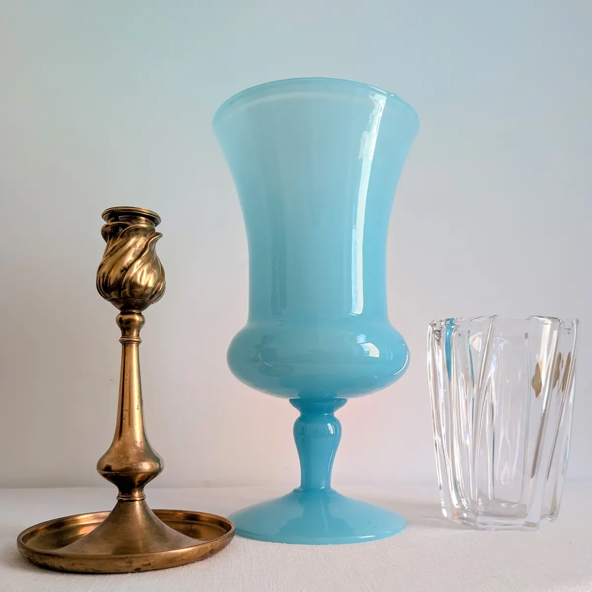 Vase Médicis opaline bleue présenté aux côtés d un bougeoir en laiton