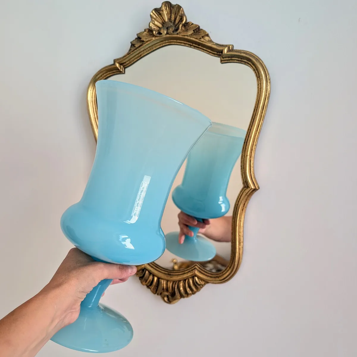 Prise en main du grand vase en opaline bleue devant un miroir doré