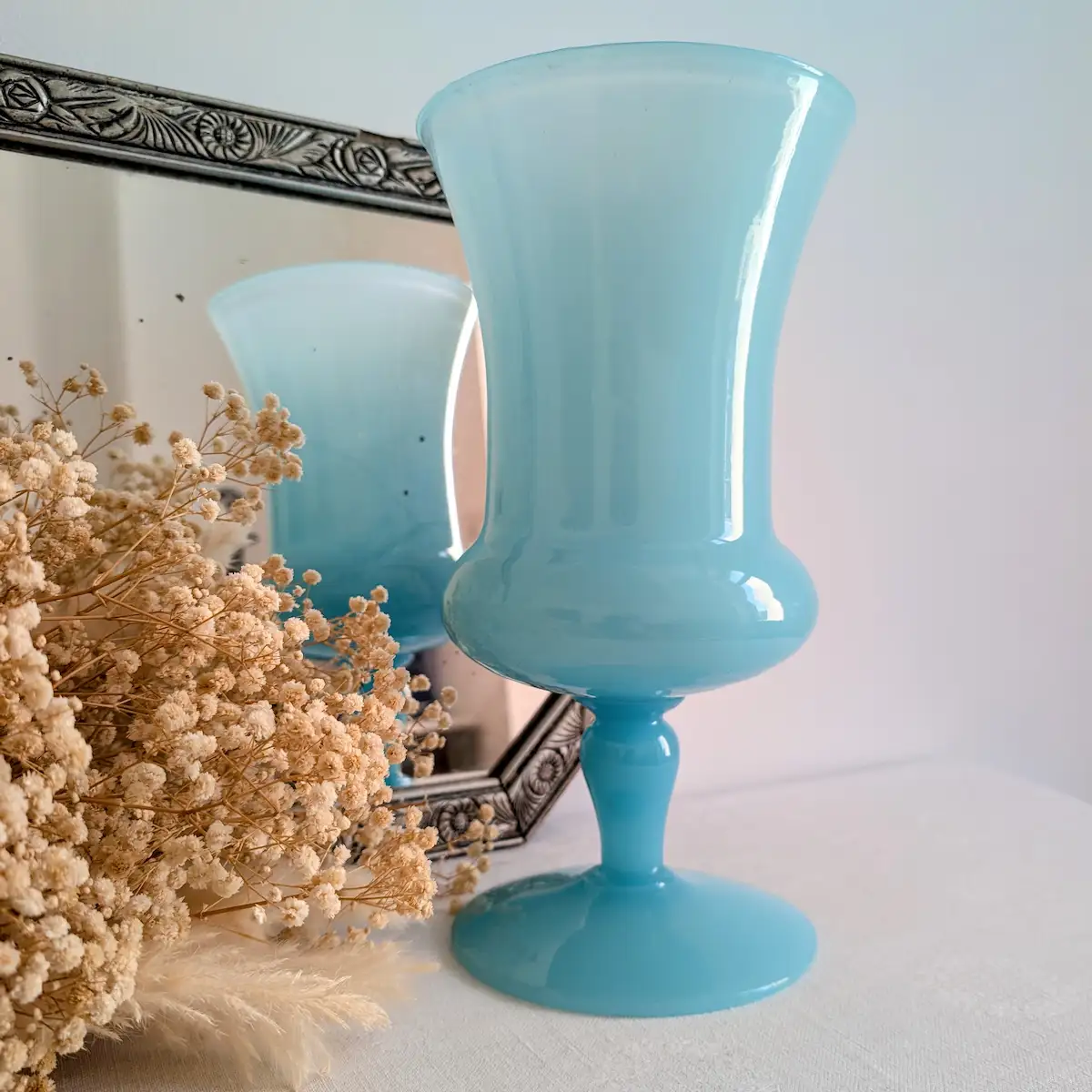 Vase opaline bleue vintage posé devant un miroir et bouquet de fleurs séchées