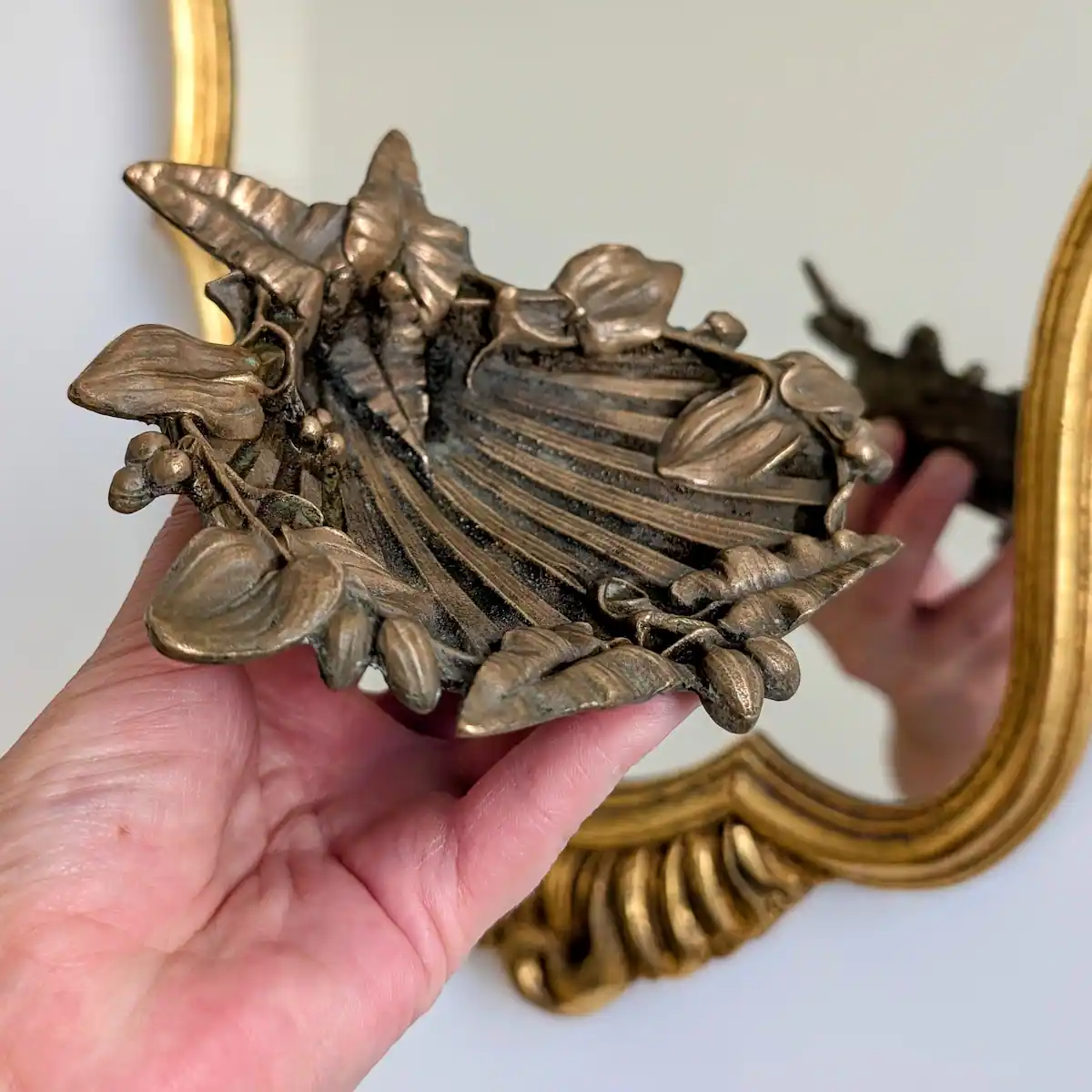 Prise en main d'un vide-poche ancien en bronze Art nouveau devant un miroir doré