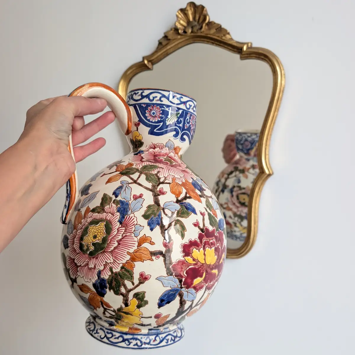 Aiguière Gien Pivoines tenue devant un miroir doré, montrant son volume et son décor floral
