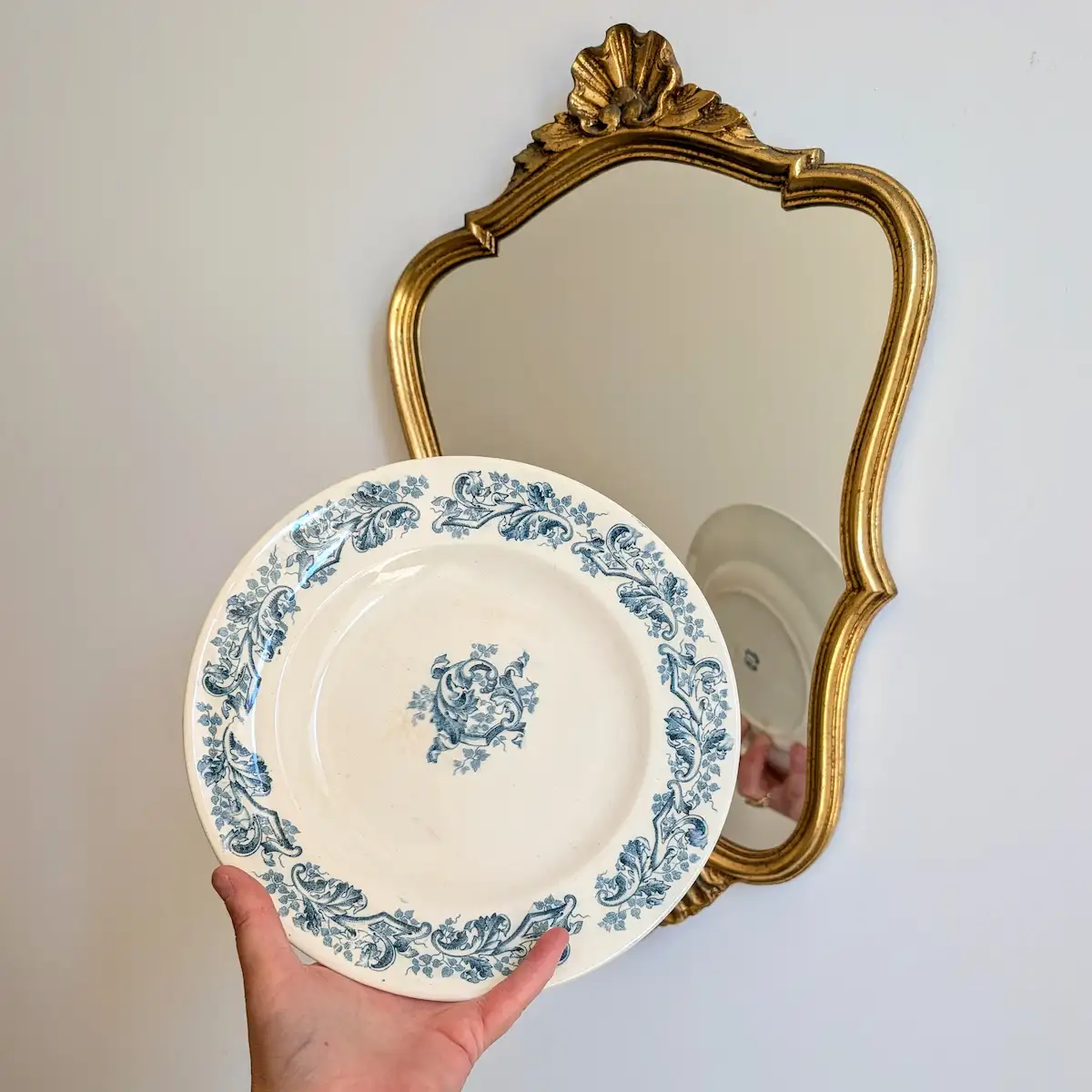 Assiette ancienne Longwy modèle Russe tenue en main devant un miroir doré