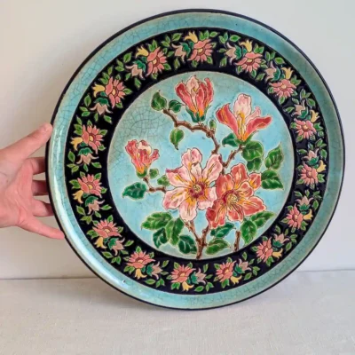 Grande assiette murale Longwy tenue en main, décor floral et bordure bleu nuit