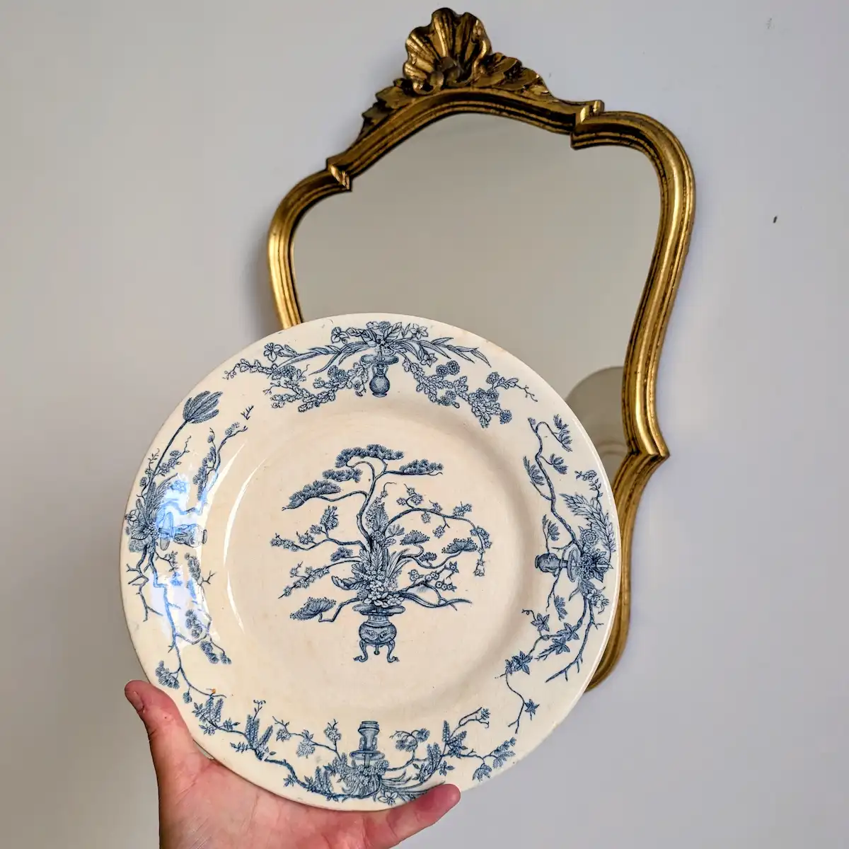 Assiette ancienne Gien modèle Yeddo tenue en main devant un miroir doré