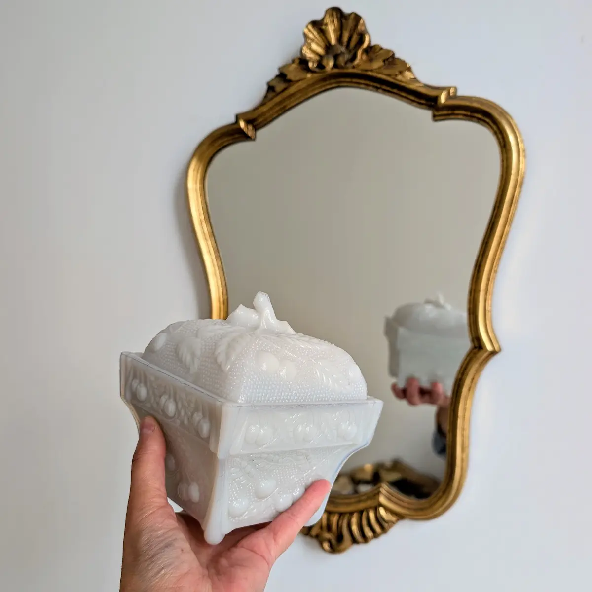 Bonbonnière ancienne en opaline blanche présentée devant un miroir doré