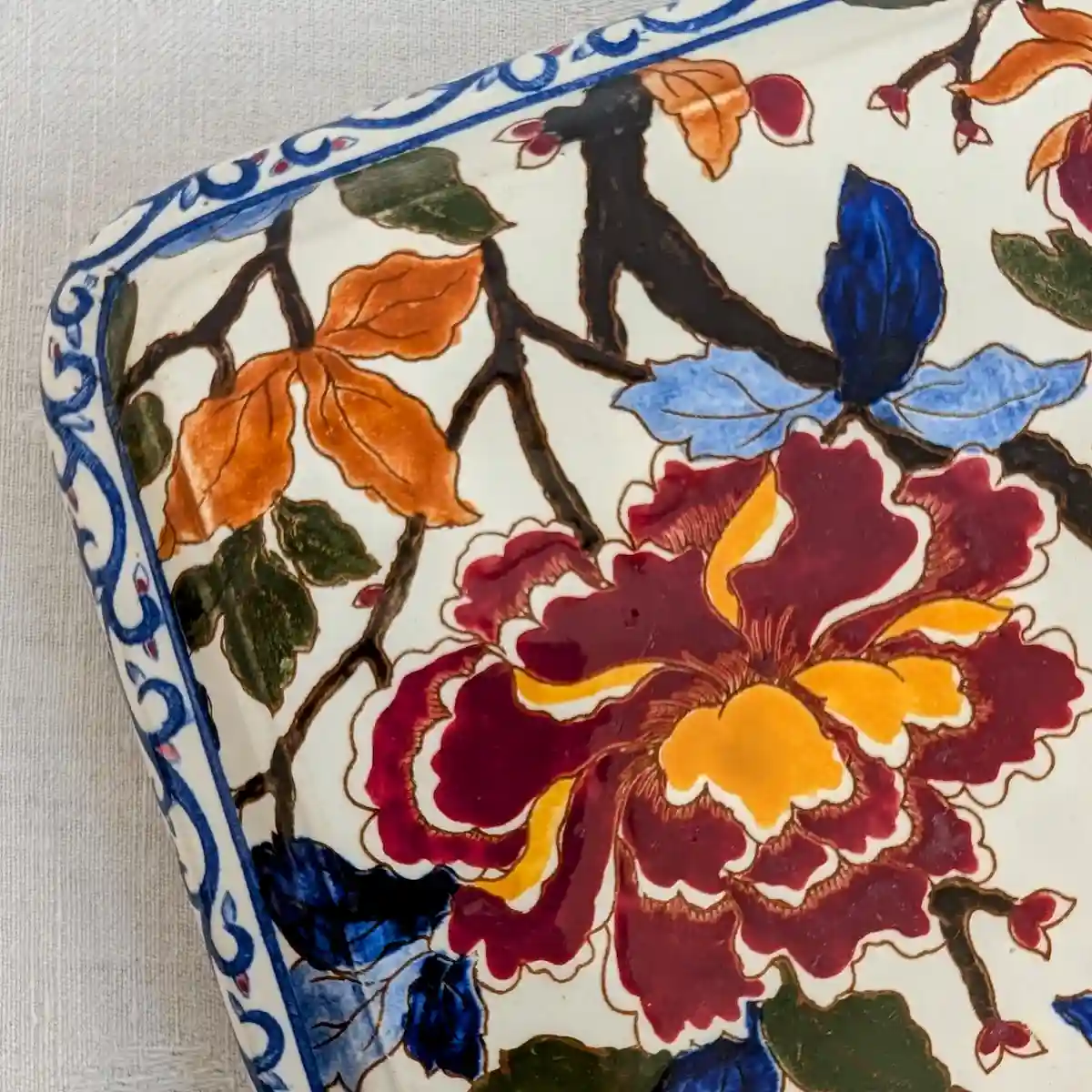 Détail d’une pivoine grenat et jaune et de la bordure bleue du dessous-de-plat Gien