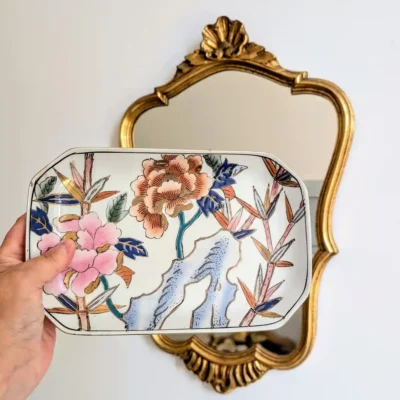 Plateau en porcelaine asiatique tenu à la main devant un miroir doré ancien.