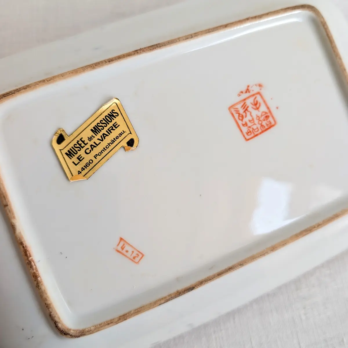Revers du plateau en porcelaine avec cachets rouges et ancienne étiquette du Musée des Missions de Pontchâteau.