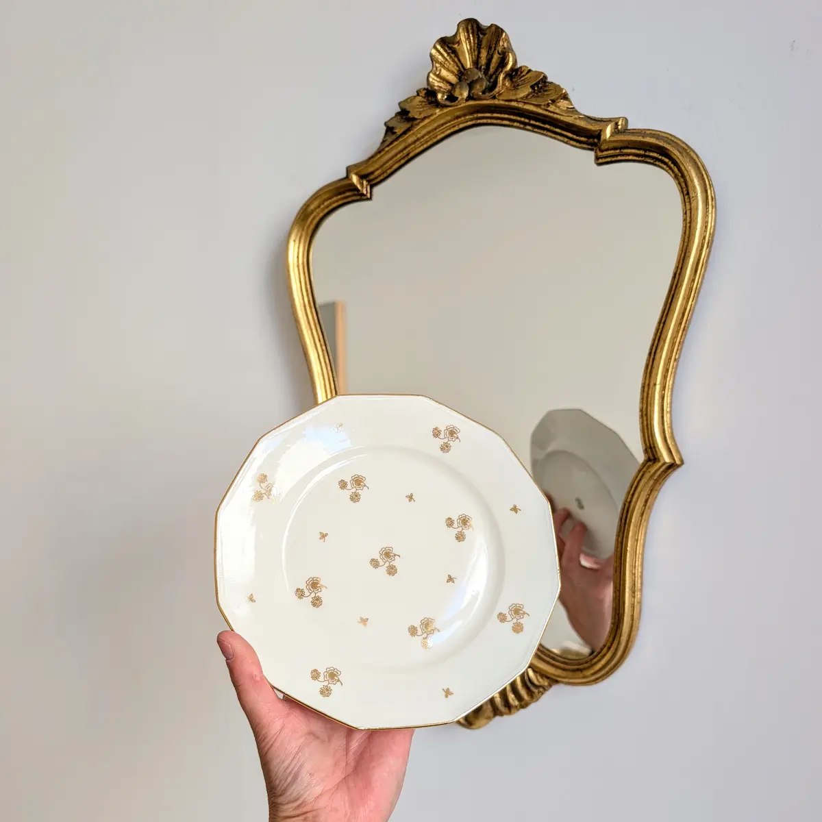 Main tenant une assiette à dessert ancienne de Limoges devant un miroir doré