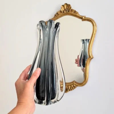 Vase Murano vintage en verre fumé tenu en main devant un miroir doré