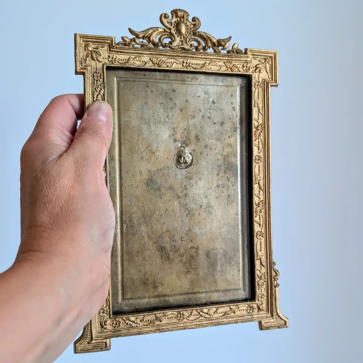 Cadre doré tenu en main, montrant ses proportions et les reliefs du décor fleuri