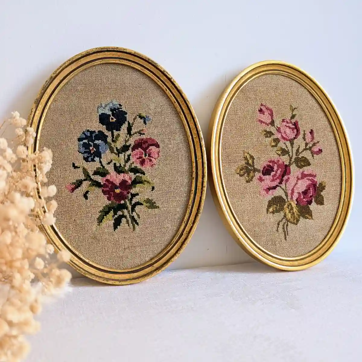 Paire de tableaux brodés aux pensées et aux roses, avec des fleurs séchées au premier plan.