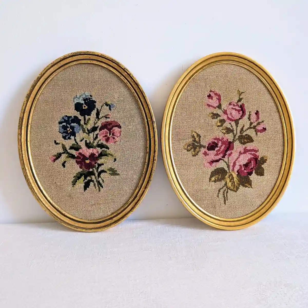 Deux cadres ovales dorés, avec pensées brodées à gauche et roses roses à droite.