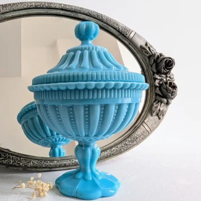 Bonbonnière opaline bleue mise en scène devant un miroir ancien