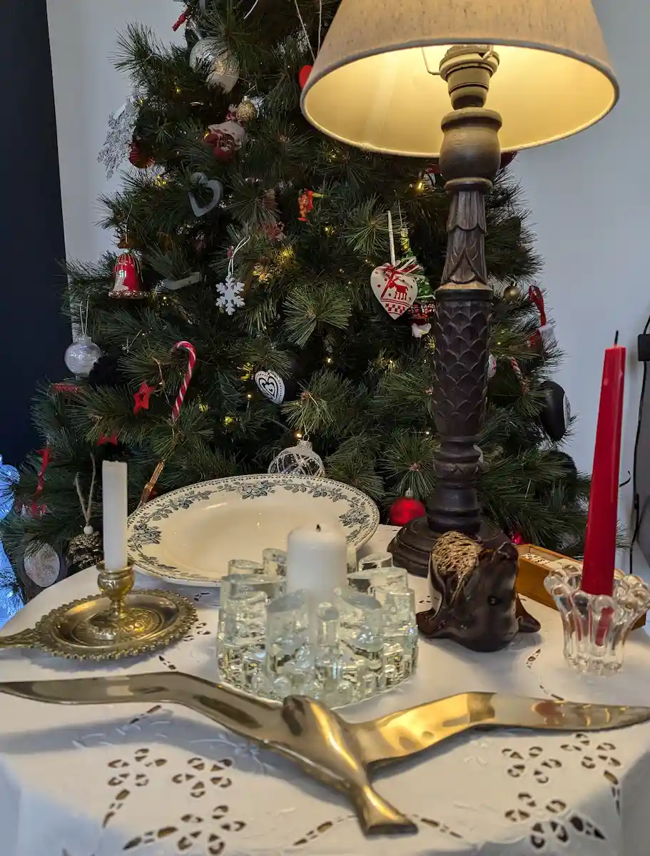 Composition d'objets chinés avec bougeoirs en verre et métal, plat ancien et lampe devant un sapin de Noël