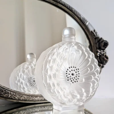Flacon Dahlia de trois quarts devant un miroir, montrant sa tranche transparente et ses pétales en relief.