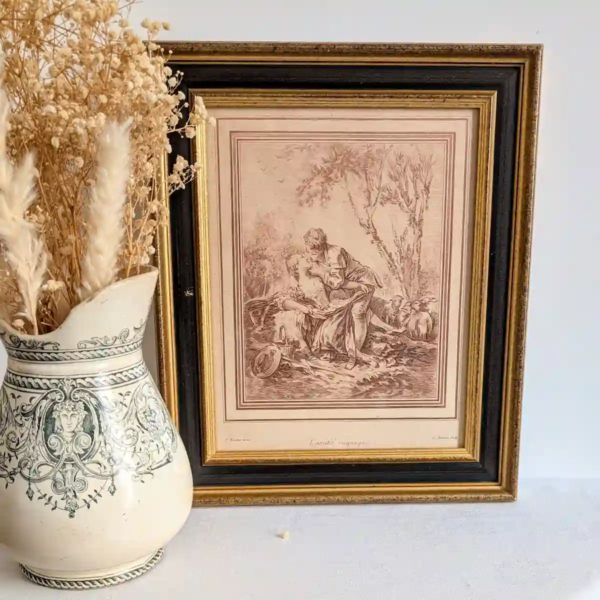 Gravure L’Amitié réciproque présentée à côté d'un vase ancien garni de fleurs séchées.