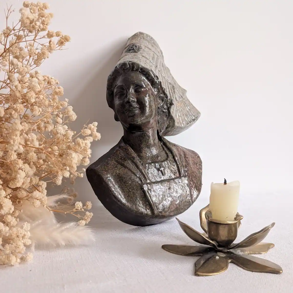 Buste de Bretonne présenté près de fleurs séchées et d’un bougeoir en forme de fleur