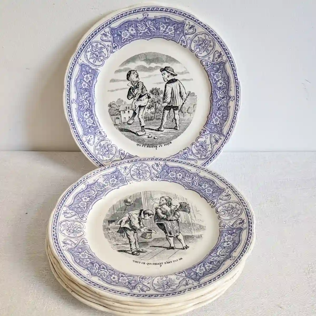 Six assiettes parlantes Digoin et Sarreguemines empilées, avec une assiette dressée illustrant le proverbe Qui s'y frotte s'y pique.