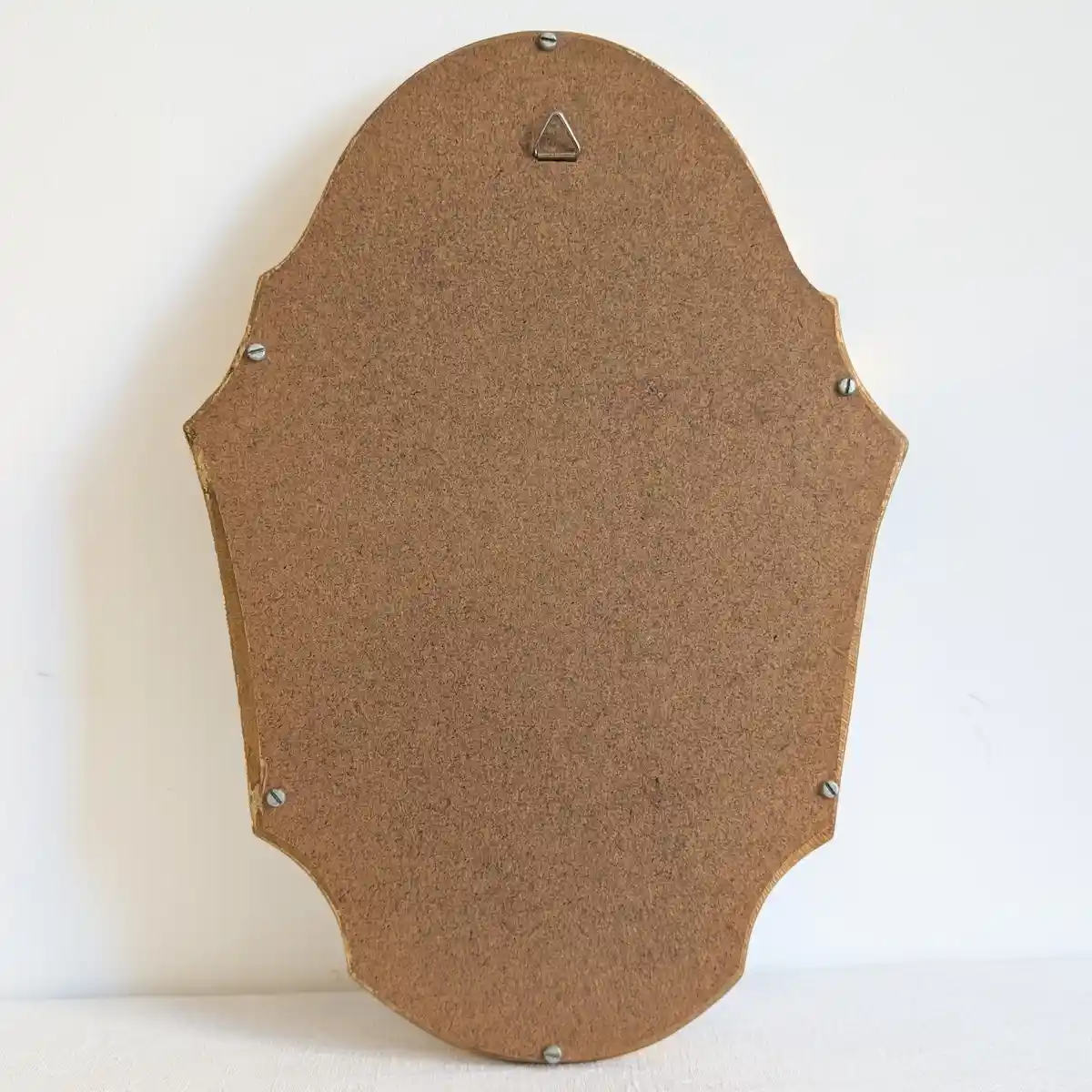 Revers du miroir fermé par un panneau brun vissé, avec une attache triangulaire en partie haute.