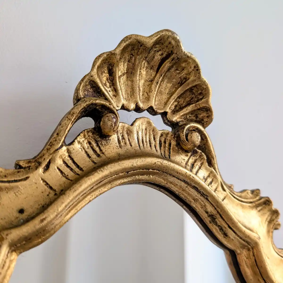 Gros plan sur la coquille supérieure et les volutes du petit miroir doré de style Louis XV.