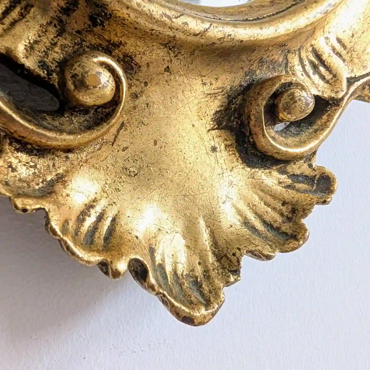 Détail de la coquille inférieure et des volutes patinées d'un miroir doré vintage.