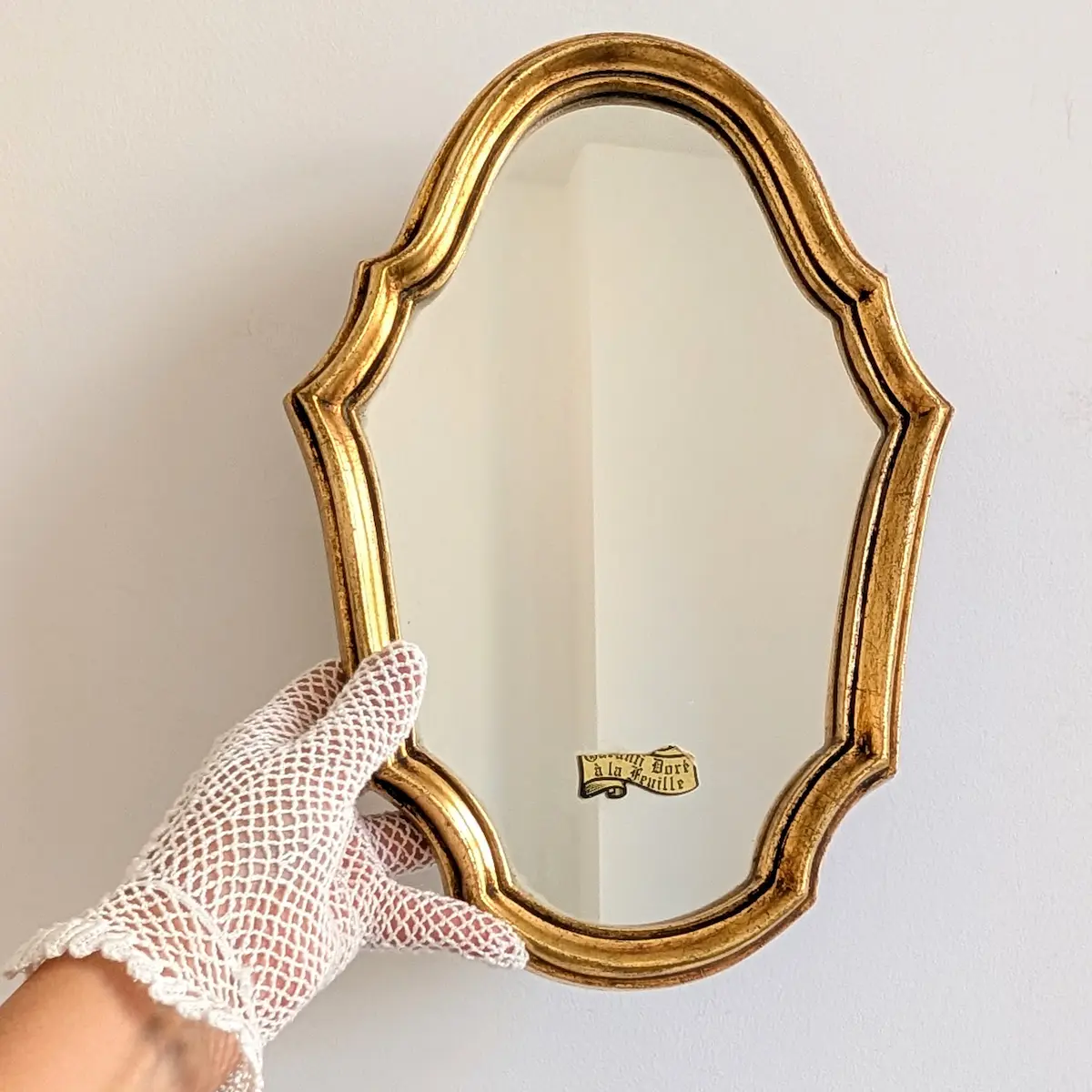 Miroir chantourné en bois doré tenu par une main gantée pour montrer ses proportions.