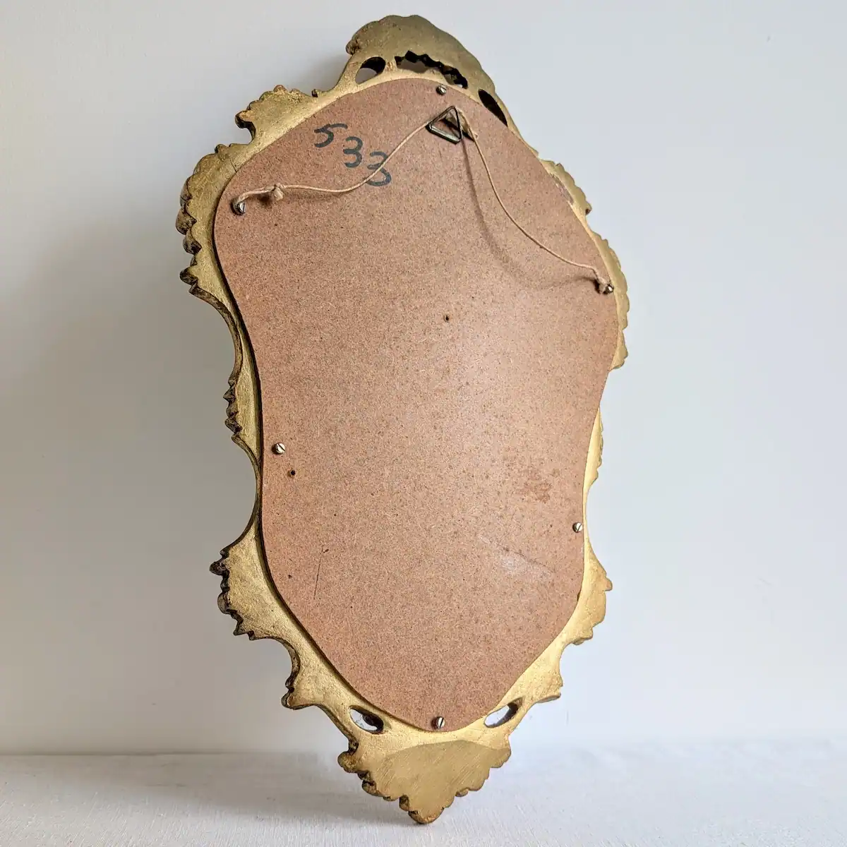 Revers du petit miroir doré vintage avec panneau de fond et fil de suspension murale.