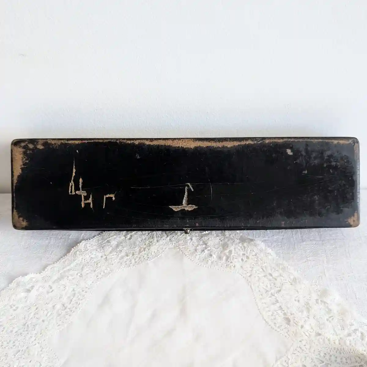 Dessous noir du plumier avec signes gravés, rayures et usure de la finition sur les bords.