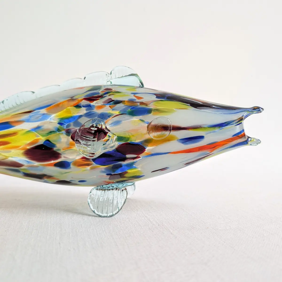 Gros plan sur la tête du poisson en verre, son œil en relief et les inclusions bleues et jaunes.