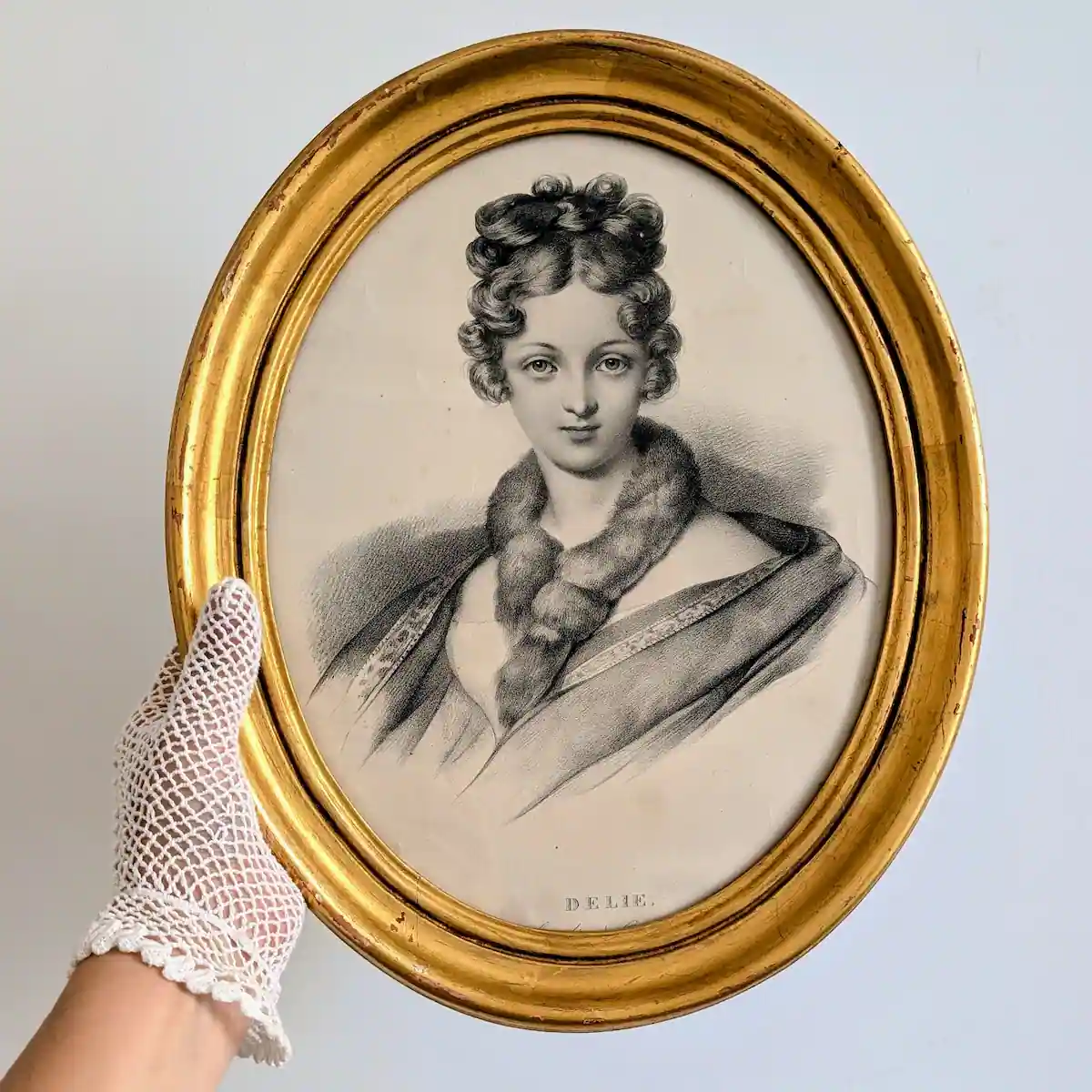 Portrait de Délie dans son cadre doré tenu par une main gantée pour montrer ses proportions.
