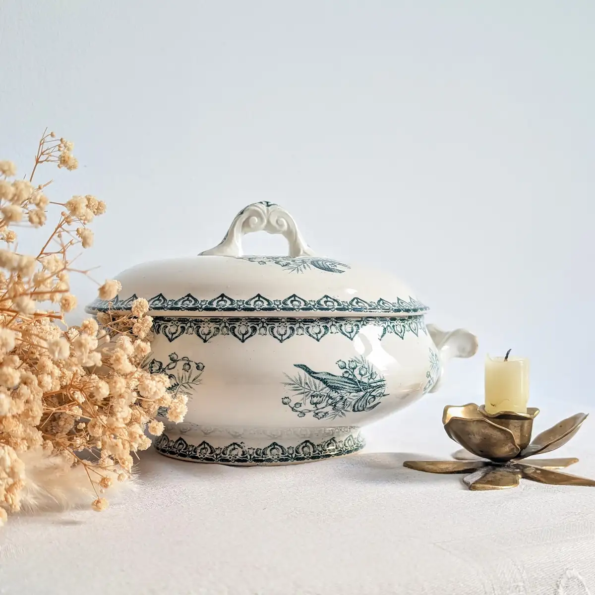Soupière en faïence verte et blanche présentée avec des fleurs séchées et un petit bougeoir.