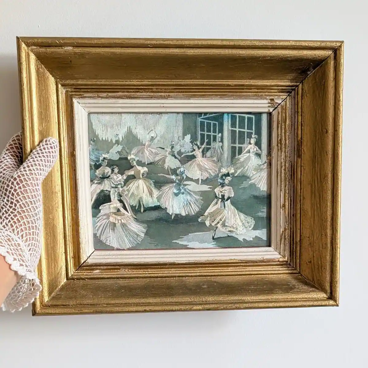 Tableau de danseuses dans son cadre doré, tenu sur le côté par une main gantée pour apprécier ses proportions.