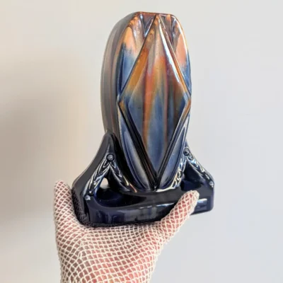 Vase Art Déco tenu dans une main gantée, vu en oblique avec ses reliefs et ses nuances bleues et ocre.